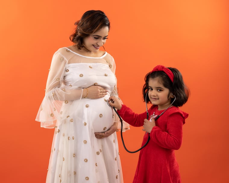 Cute Daughter of Pregnant Indian Woman Using Stethoscope to Hear Baby's