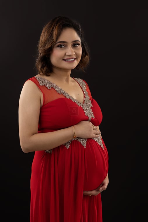 Happy Nepali mothertobe in a red saree, holding her pregnant belly